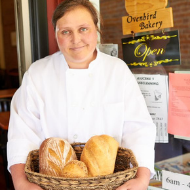 Ovenbird Bakery baker holding basket of bread in front of sign